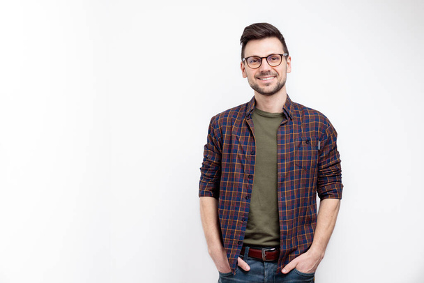 Unshaved charming cheerful positive young man in glasses hold hands pockets isolated on white background - Fotografie, Obrázek