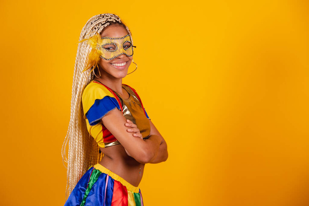 beautiful black Brazilian woman, dressed in carnival clothes, mask. yellow background. crossed arms. - 写真・画像