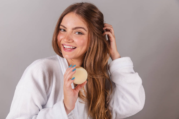 beautiful brazilian woman dressed in bathrobe, holding a soap for skin care. posing for photo. - Foto, afbeelding