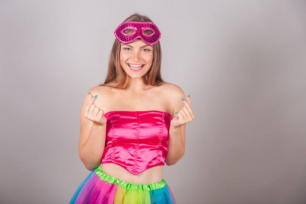 Brazilian blonde woman dressed in pink carnival clothes. wearing mascara, heart sign with fingers. - Foto, Imagem