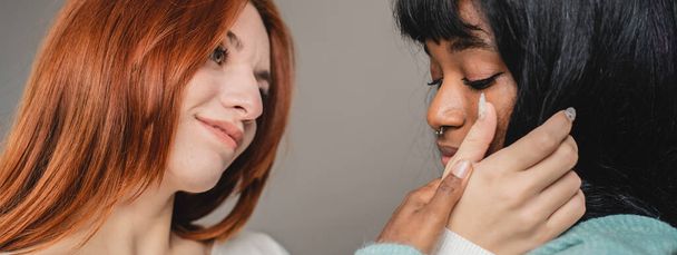 Horizontal banner with couple of young lesbian women of different ethnicities - Red headed Caucasian woman and African american girlfriend caressing each other - lgbtq and gay couple rights concept - Photo, Image
