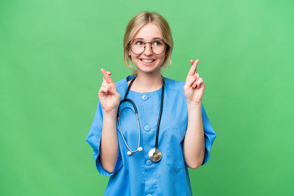 Young nurse English woman over isolated background with fingers crossing - Foto, Imagem