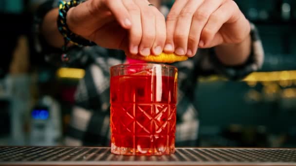 barman knijpen een stuk sinaasappelschil en garnering negroni cocktail aan de bar close-up - Video