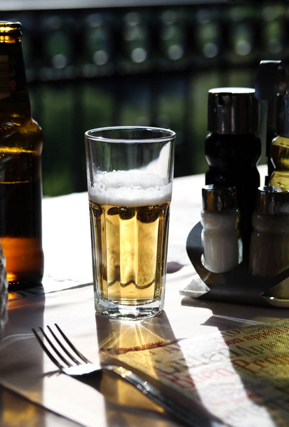 Un vaso de cerveza fría con espuma en la mesa del restaurante. Fotografía de la vida real en un restaurante, día soleado, cerveza fría sobre la mesa, primer plano, espacio para copiar. - Foto, imagen