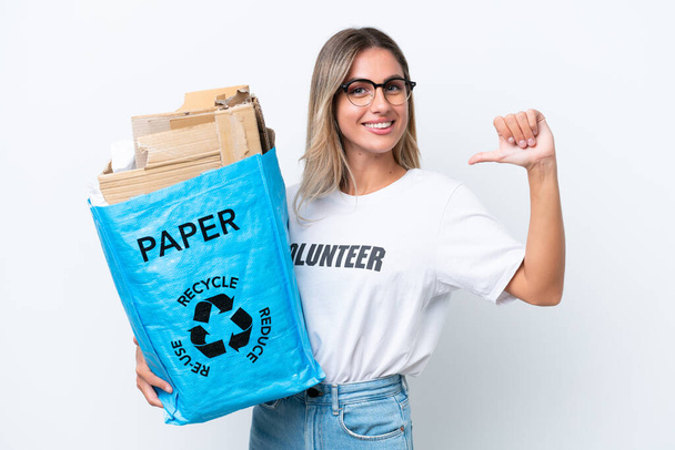 Νεαρή όμορφη Ουρουγουανή γυναίκα που κρατάει μια σακούλα ανακύκλωσης γεμάτη χαρτί για να ανακυκλώσει απομονωμένη σε λευκό χρωματικό υπόβαθρο περήφανη και αυτάρεσκη - Φωτογραφία, εικόνα