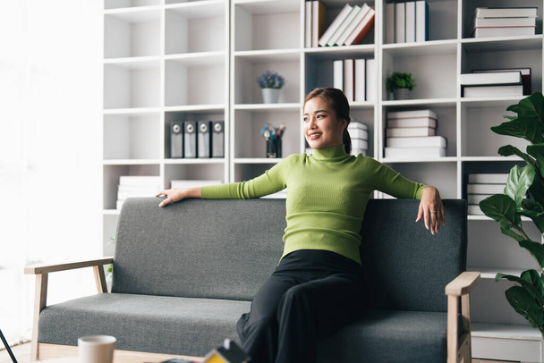 Almeja millennial asiático chica sentarse resto en sofá en sala de estar. Feliz joven mujer relajarse en cómodos muebles de sofá en casa. - Foto, Imagen