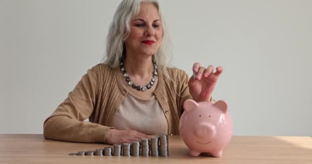 Ältere Frau legt Münze in Sparschwein. Altersvorsorge und Versicherungen - Filmmaterial, Video