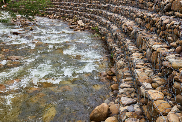 Укрепление берегов горной реки, сетки и камней. Пейзаж берега реки и большие камни с металлической сеткой - Фото, изображение