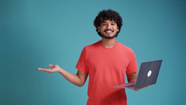 Photo of young successful entrepreneur influencer Indian finger point empty space recommend laptop new ad isolated on blue studio background - 写真・画像