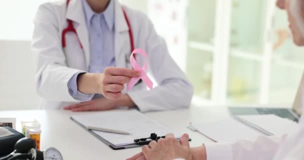 Il medico mammologo tiene il nastro rosa e lo passa alla donna anziana in clinica. Simbolo internazionale di coloro che sostengono la lotta contro il cancro al seno - Filmati, video