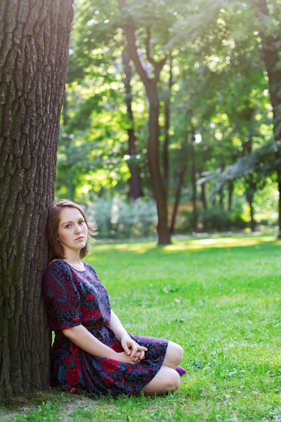 Sad young woman sitting under a tree - Фото, изображение