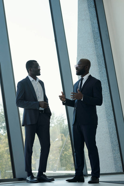 Jovem confiante afro-americano masculino empregado em terno elegante explicando algo ao colega em reunião no centro de escritório - Foto, Imagem