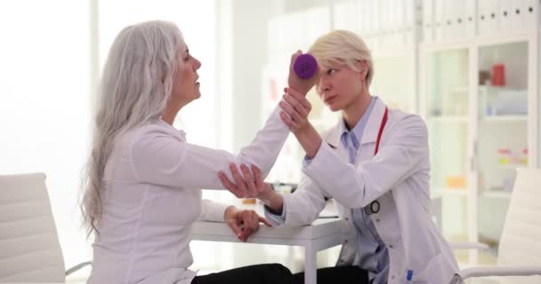 Dambılı ve fizyoterapi rehabilitasyonu hemşiresi olan yaşlı bir kadın fitness ve kas desteğine yardımcı oluyor. Yaşlı bir hastanın eliyle tıbbi fizyoterapist. - Video, Çekim