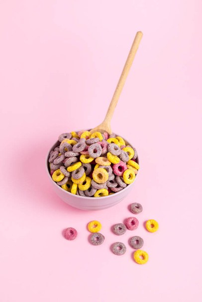 Bol de céréales colorées avec une cuillère sur un fond rose - Photo, image