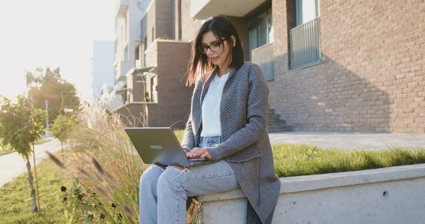 Attractive caucasian busy woman sitting on street during break time working and typing text on laptop. Outdoors - Фото, изображение