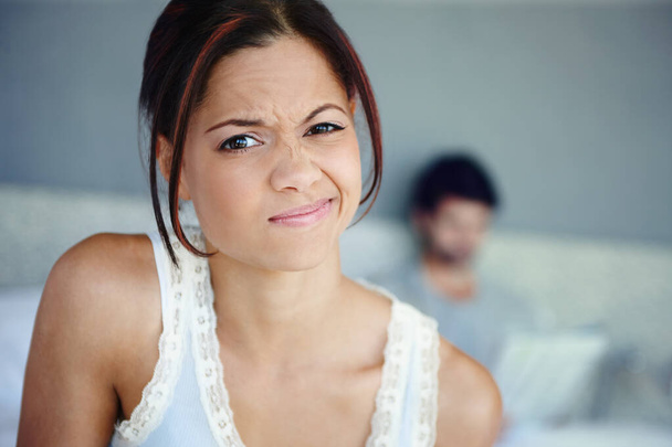 Im not impressed. Portrait of a woman scrunching up her face sitting in her bedroom with her boyfriend in the background - Fotoğraf, Görsel