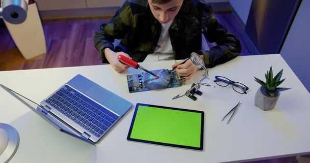 Unknown male hands soldering using soldering iron and screwdriwer on the table at home. green screen digital tablet. Engineer soldering microcircuit. - Φωτογραφία, εικόνα