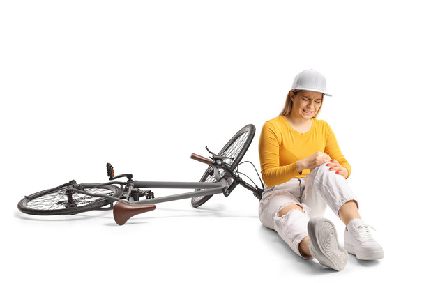 Young female with a bicycle sitting on the floor and holding her painful knee isolated on white background - Foto, Imagem