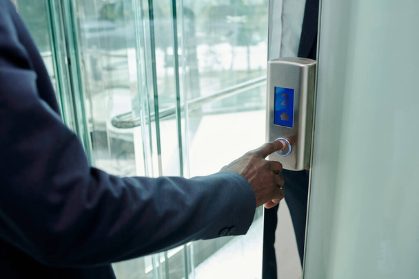 Kéz a fiatal afro-amerikai üzletember nyomja meg a hívógombot panelen átlátszó üvegajtó lift modern irodai központ - Fotó, kép