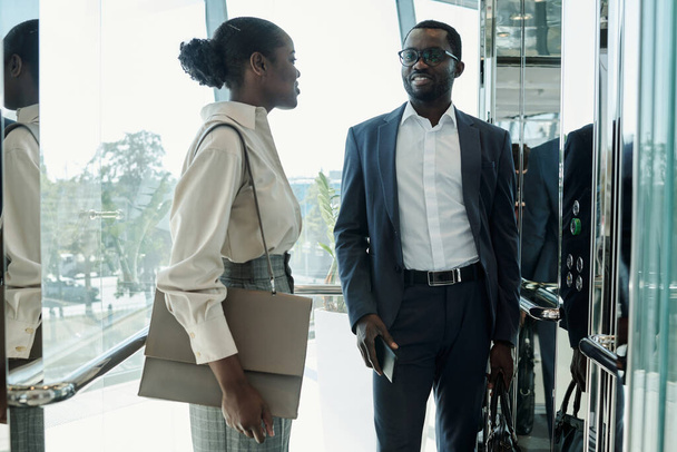 Jovem mulher elegante com bolsa e seu colega de terno tendo discussão de alguns pontos de trabalho no elevador em movimento - Foto, Imagem