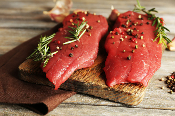 Raw beef steak with rosemary and spices on cutting board on wooden background - Foto, afbeelding