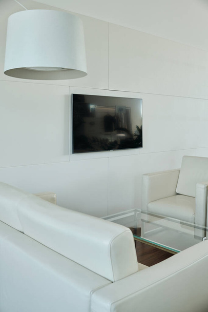 Parte della zona di ricarica in moderno ufficio openspace con divano in pelle bianca e poltrona che circonda tavolino di vetro da parete - Foto, immagini