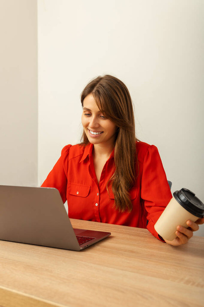 Pionowe ujęcie kobiety pracującej przy biurku na laptopie i pijącej kawę w swoim biurze. - Zdjęcie, obraz