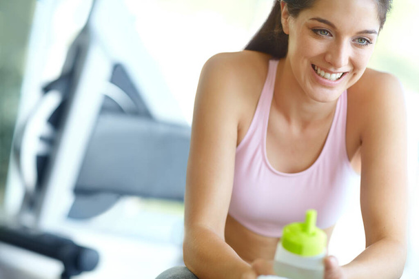 This has been a great workout. A beautiful young woman sitting at the gym taking a break and having a drink of water - 写真・画像