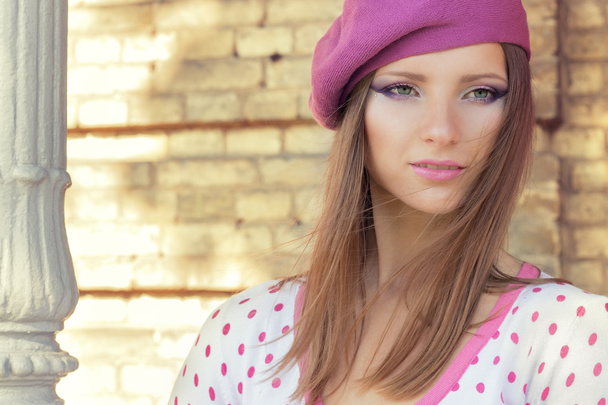 Menina sexy bonita em um chapéu rosa com bela maquiagem na jaqueta branca em pontos de bolinhas rosa fica em um dia de outono ensolarado no parque perto de folhas vermelhas
 - Foto, Imagem