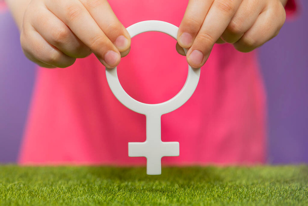 The concept of gender. Female gender symbol in hand on purple background in pink t-shirt with copy space. High quality photo - Photo, Image