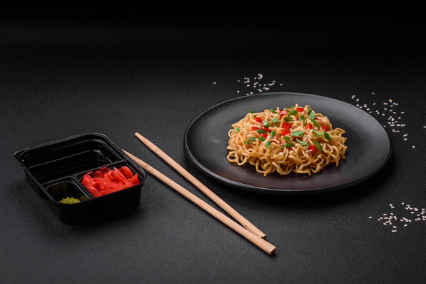 Νόστιμα φρέσκα ασιατικά noodles με λαχανικά, αλάτι, μπαχαρικά και βότανα σε κεραμικό πιάτο σε σκούρο μπετόν φόντο - Φωτογραφία, εικόνα