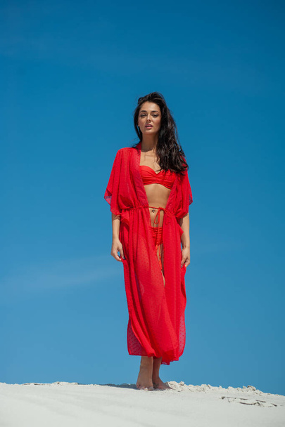 beautiful young woman in a red dress posing on the beach - Фото, зображення