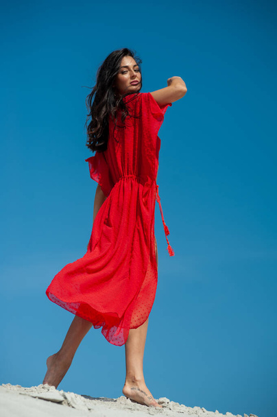 όμορφη νεαρή γυναίκα με ένα κόκκινο φόρεμα ποζάροντας στην παραλία - Φωτογραφία, εικόνα