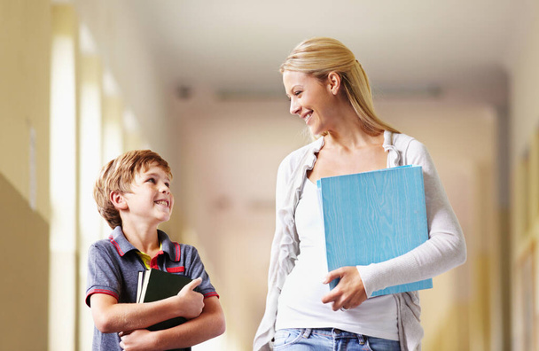 Talking, teacher and boy walking, hallway and happiness with advice, help and education. Male child, student and woman with a smile, lobby and conversation with joy, communication and development. - Photo, image