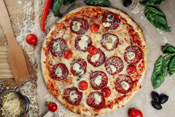 Pizza com queijo de frango e pepperoni, um pedaço do qual é cortado e colocado como um pakman, está em uma tábua de madeira e um fundo marrom. Queijo espalha estrias fluindo. Foto de alta qualidade - Foto, Imagem