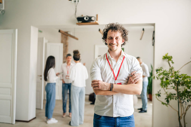 Портрет взрослого мужчины перед коллегами портрет белый мужчина стоять на работе счастливая улыбка уверенно с вьющимися современными волосами носить белую рубашку копия пространства яркий фильтр - Фото, изображение
