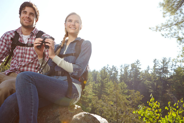 Taking in the beautiful scenery. A young couple atop a mountain while holding their binoculars - Photo, Image