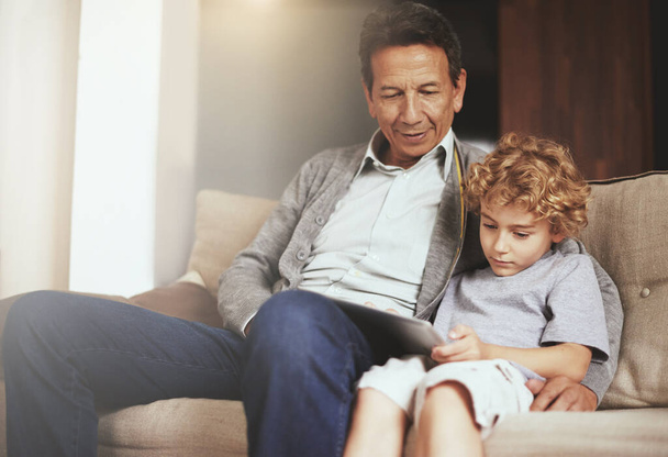 Tablet, Kind oder Großvater streamen Filme oder Filme über ein Online-Abo im Ruhestand zu Hause, um sich zu entspannen. Kind, Großeltern oder Kind schauen gerne lustige Videos mit einem älteren oder reifen alten Mann auf dem Sofa. - Foto, Bild