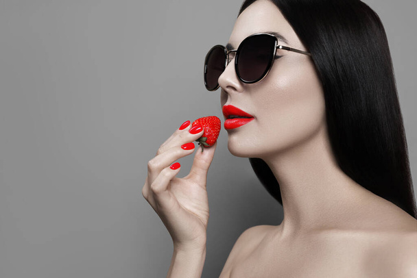 Attractive woman in stylish sunglasses holding strawberry on grey background, space for text. Color accent - Fotó, kép
