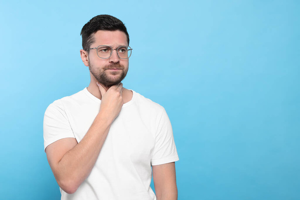 Man suffering from sore throat on light blue background, space for text - Photo, image