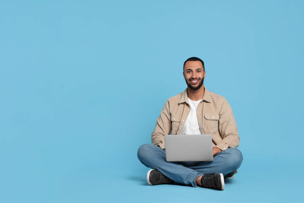 Smiling young man with laptop on light blue background, space for text - Fotó, kép