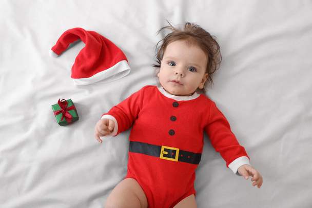 Cute baby wearing festive Christmas costume near gift box on white bedsheet, top view - Photo, image