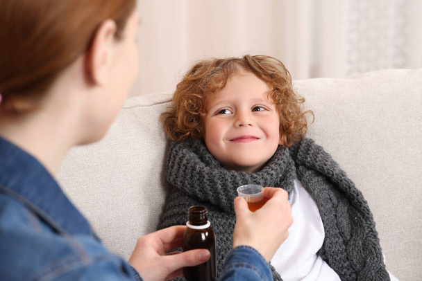 Mother giving cough syrup to her son on sofa - Foto, Bild