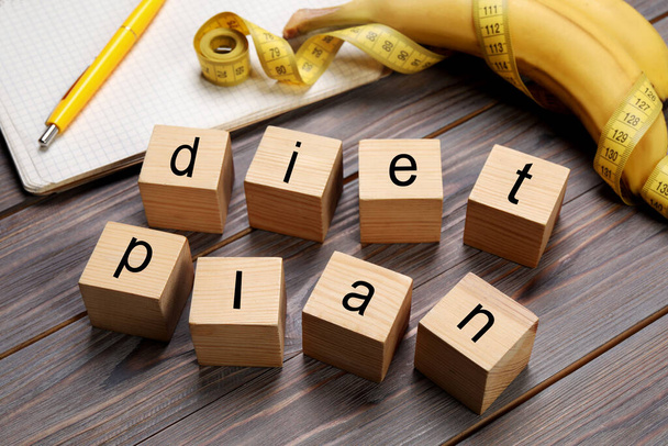 Phrase Diet Plan made of cubes, measuring tape and bananas on grey wooden table. Weight loss program - Foto, Imagen