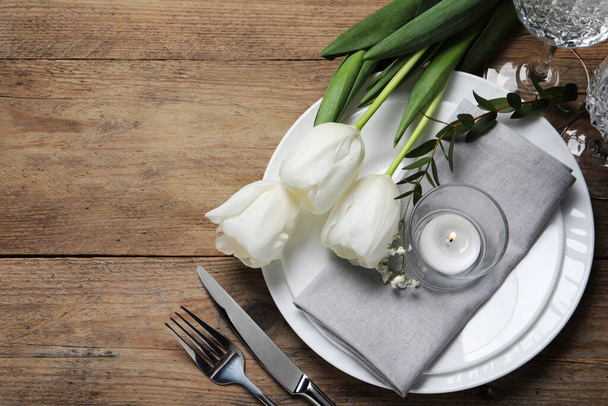 Stylish table setting with cutlery, burning candle and tulips on wooden background, flat lay. Space for text - Foto, Bild