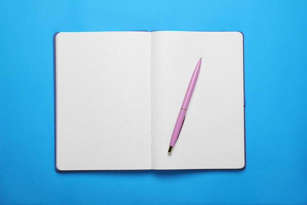 Open notebook and pen on light blue background, top view - Fotó, kép