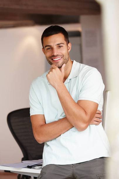 Real and reliable. Portrait of a casual young man leaning against his desk - 写真・画像
