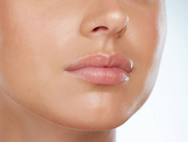 Closeup of perfect lips on unknown woman in studio. Caucasian model with smooth glowing skin isolated against a grey background and posing. Woman with healthy luscious plump lips and routine lip care. - Fotó, kép