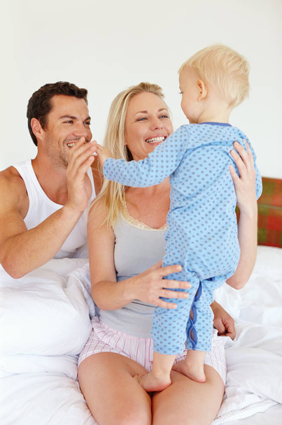 Waking up to our favourite smile. Two parents playing lovingly with their young son on their bed - Zdjęcie, obraz