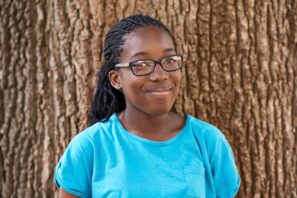 Shes not a tree hugger but she sure loves em. Portrait of a pretty black teen smiling while standing against a tree - Fotografie, Obrázek